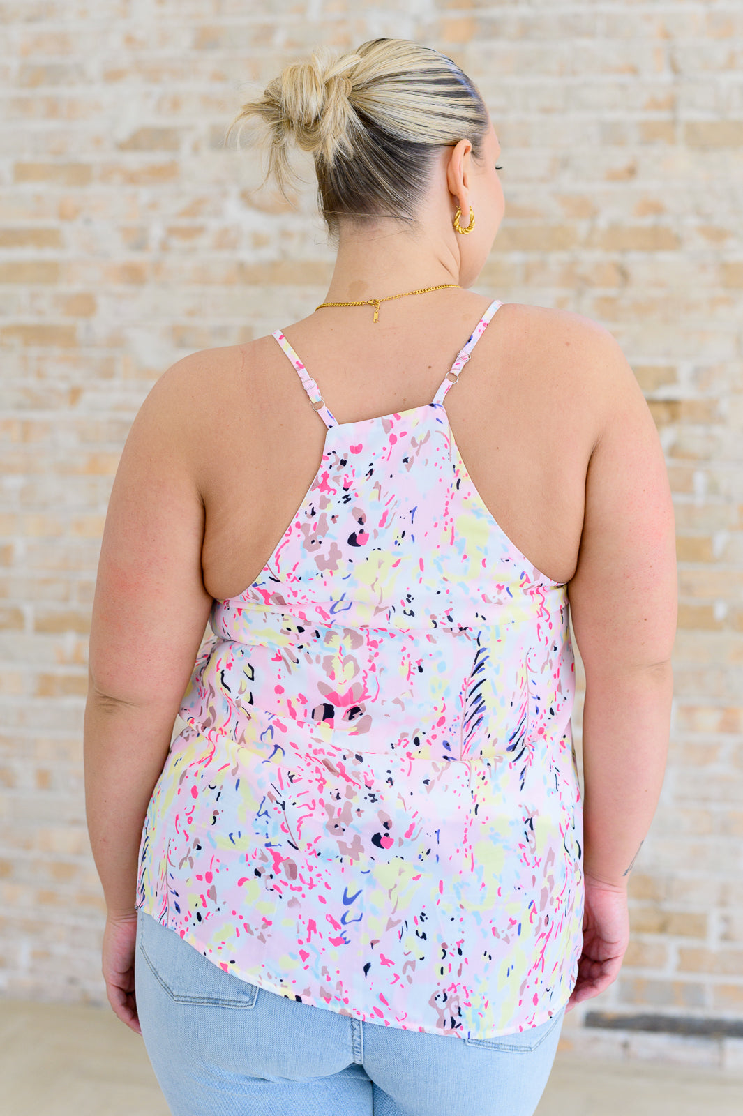 A woman wearing a multicolor printed camisole top with a v-neckline and adjustable straps, paired with high-rise straight jeans.
