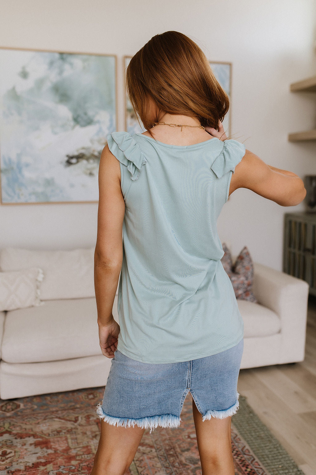 Woman in a light blue sleeveless top and denim shorts standing in a living room.