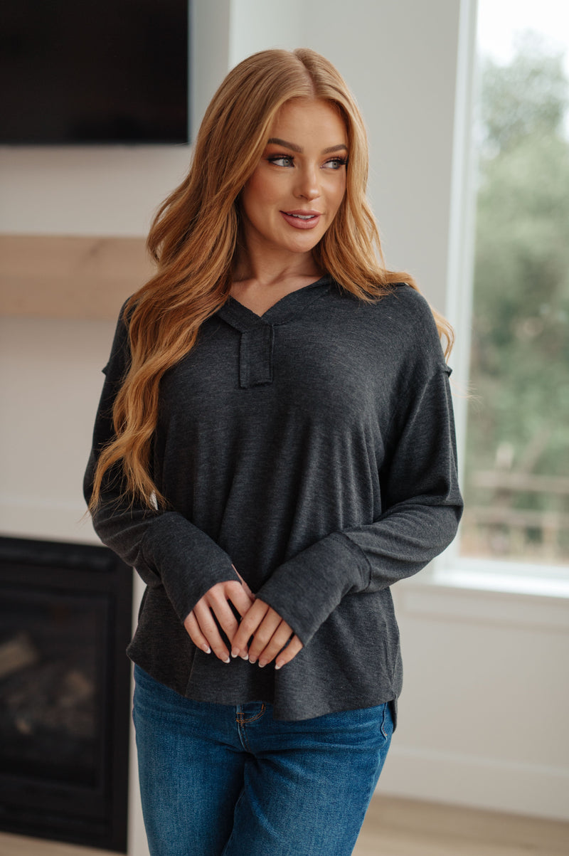 Woman wearing a dark gray sweater and blue jeans indoors.