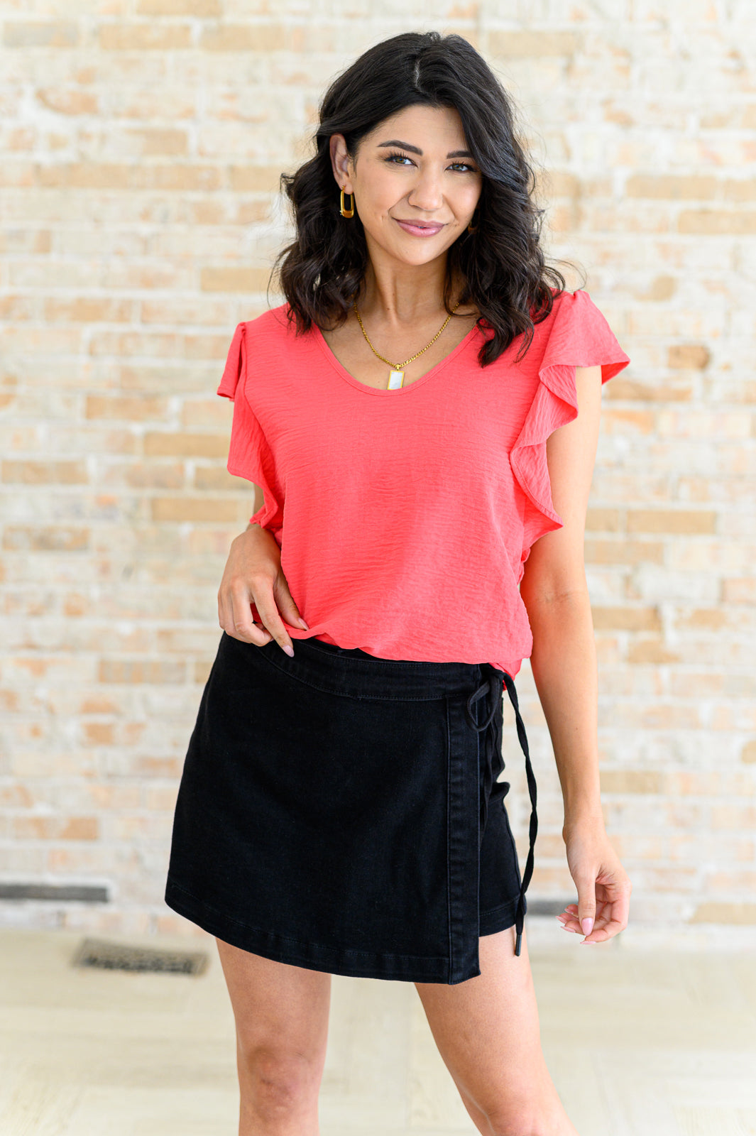 Woman wearing a coral top and black skirt against a textured wall.