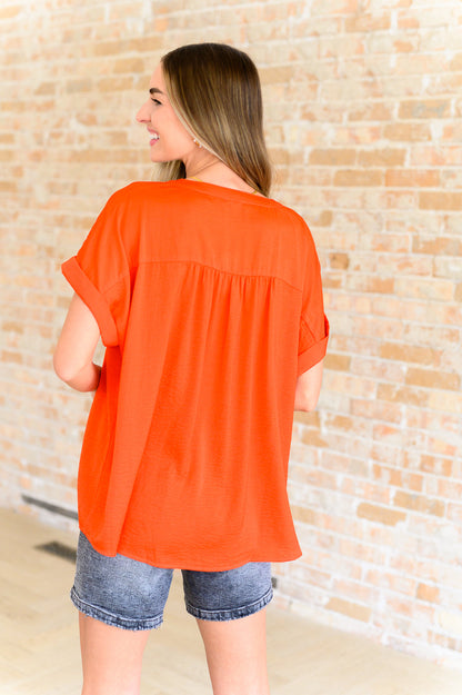 Woman wearing an orange top and denim shorts against a textured wall.