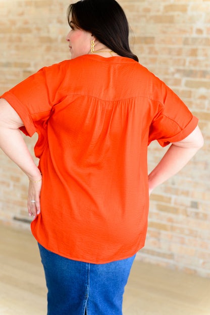 Person wearing an orange shirt and blue jeans against a brick wall.