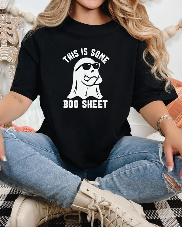 Person wearing a black t-shirt with a ghost graphic and text, sitting on a checkered floor.