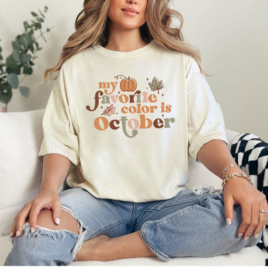 Person wearing a white t-shirt with 'my favorite color is October' text, sitting on a couch.