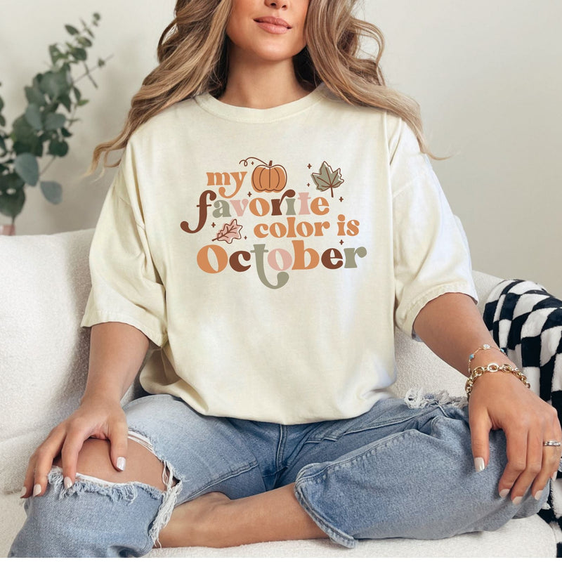Person wearing a white t-shirt with 'my favorite color is October' text, sitting on a couch.