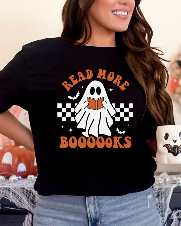 Person wearing a black t-shirt with a ghost holding a book design, surrounded by Halloween decorations.