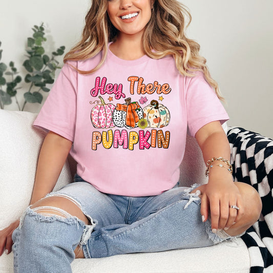 Woman wearing a pink t-shirt with 'Hey There Pumpkin' text and graphics, sitting on a couch.