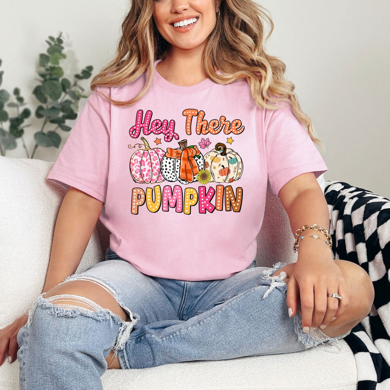 Woman wearing a pink t-shirt with 'Hey There Pumpkin' text and graphics, sitting on a couch.