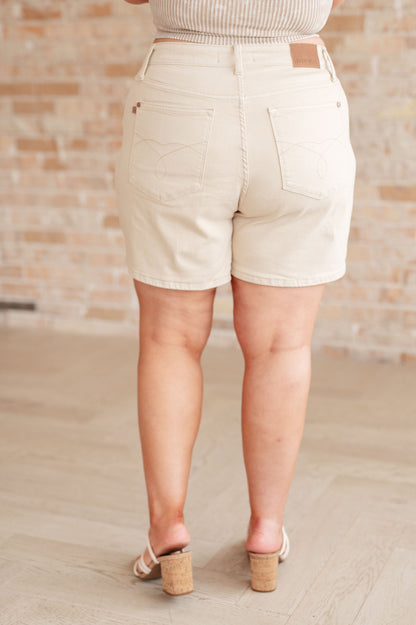 A woman is standing in a room wearing beige high-rise garment dyed shorts and a gray sleeveless 