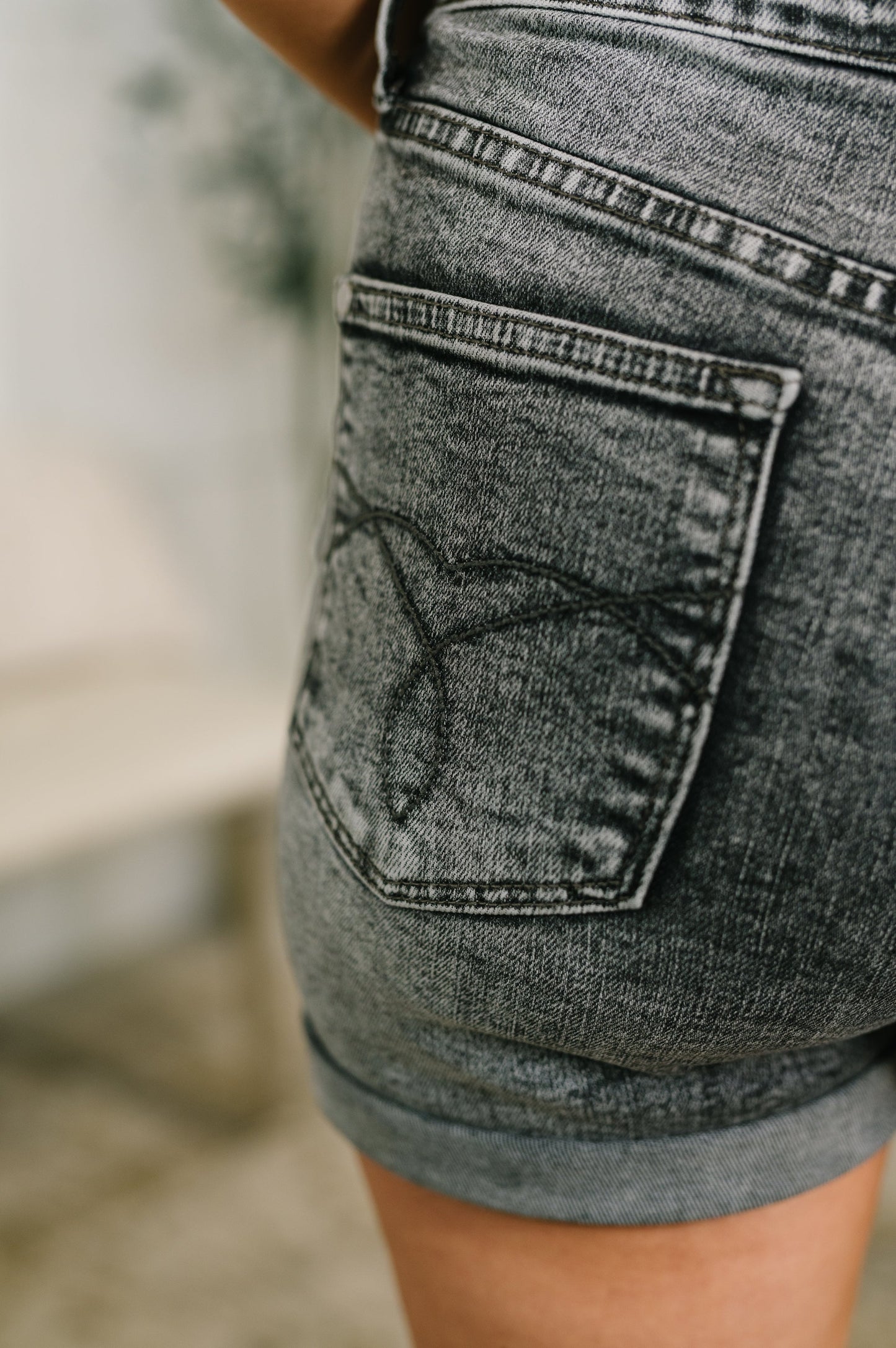 Close-up of a person wearing gray denim shorts with a blurred background