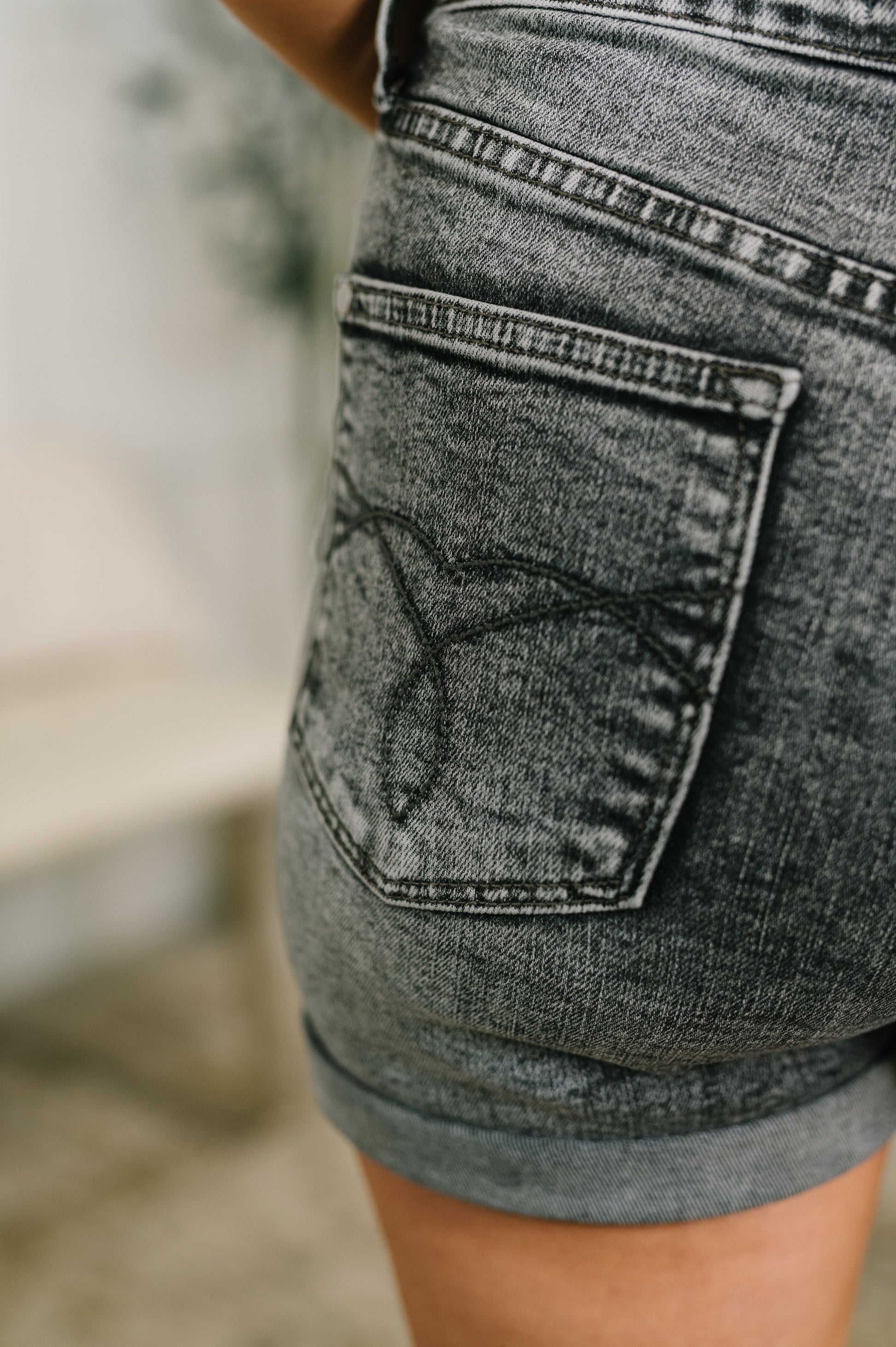 Close-up of a person wearing gray denim shorts with a blurred background