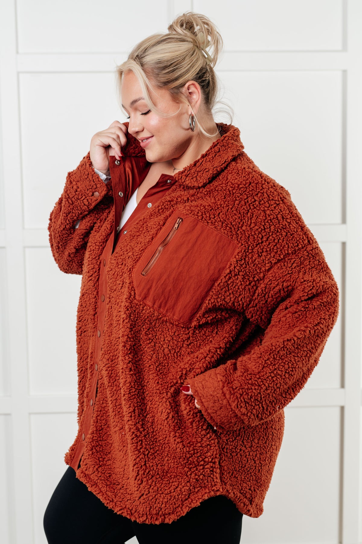 Woman wearing a rust-colored fleece jacket against a white tiled wall.
