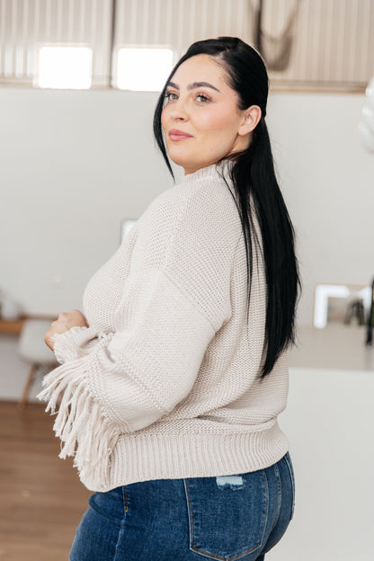 Woman wearing a beige sweater with tassels in a living room setting