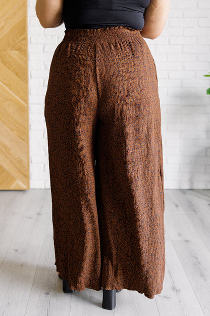 Brown wide-leg pants worn by a person against a white brick wall.
