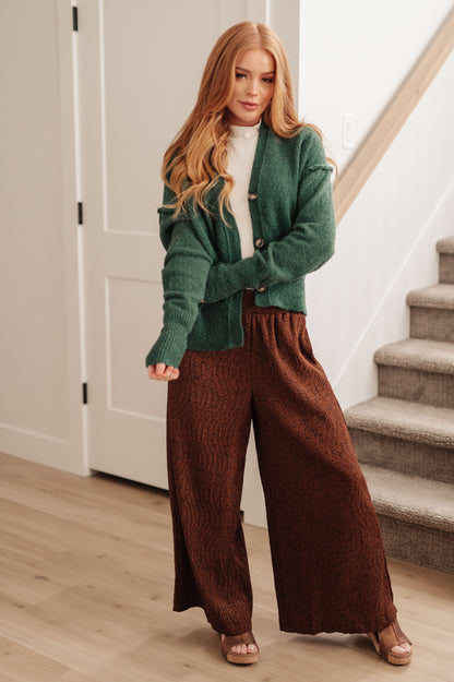 Woman wearing a green cardigan and brown pants standing in a home setting.