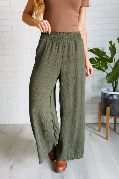 Person wearing olive green wide-leg pants with a white brick wall background