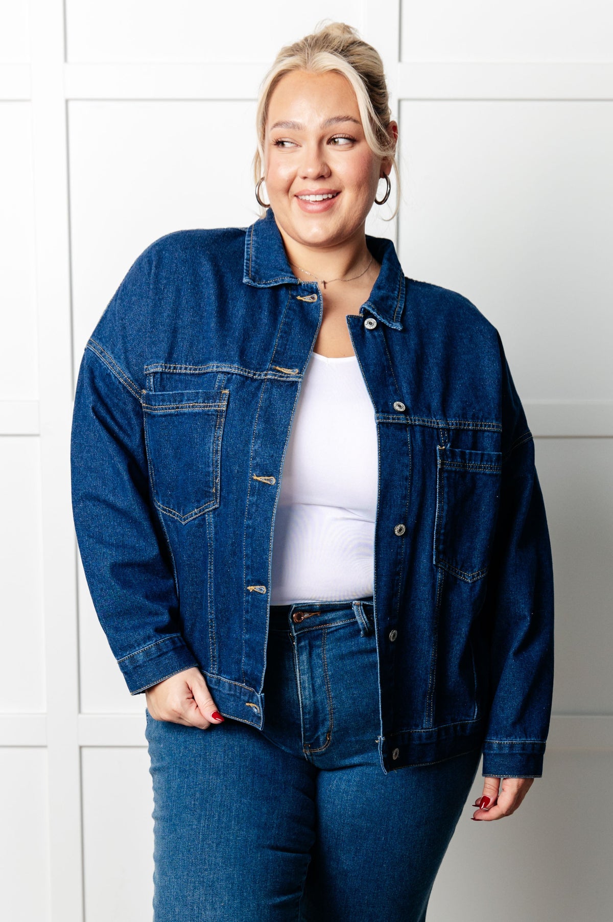 Woman wearing a blue denim jacket and jeans against a white tiled wall.
