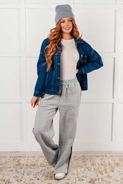 Woman wearing a denim jacket, gray beanie, and gray sweatpants against a white wall.