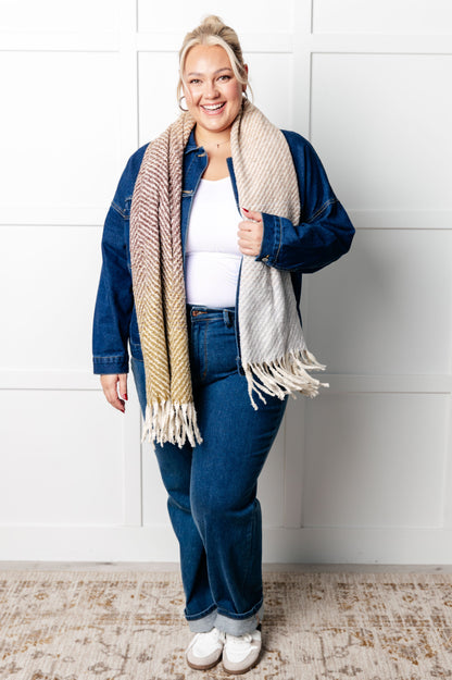 Woman wearing a denim jacket, white top, and blue jeans with a beige scarf against a white wall.