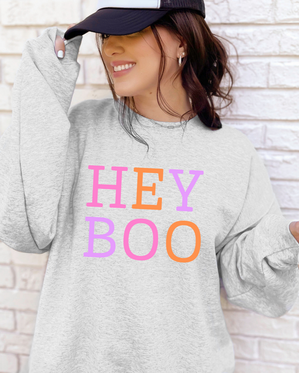 Person wearing a gray sweatshirt with 'HEY BOO' text in colorful letters against a brick wall.
