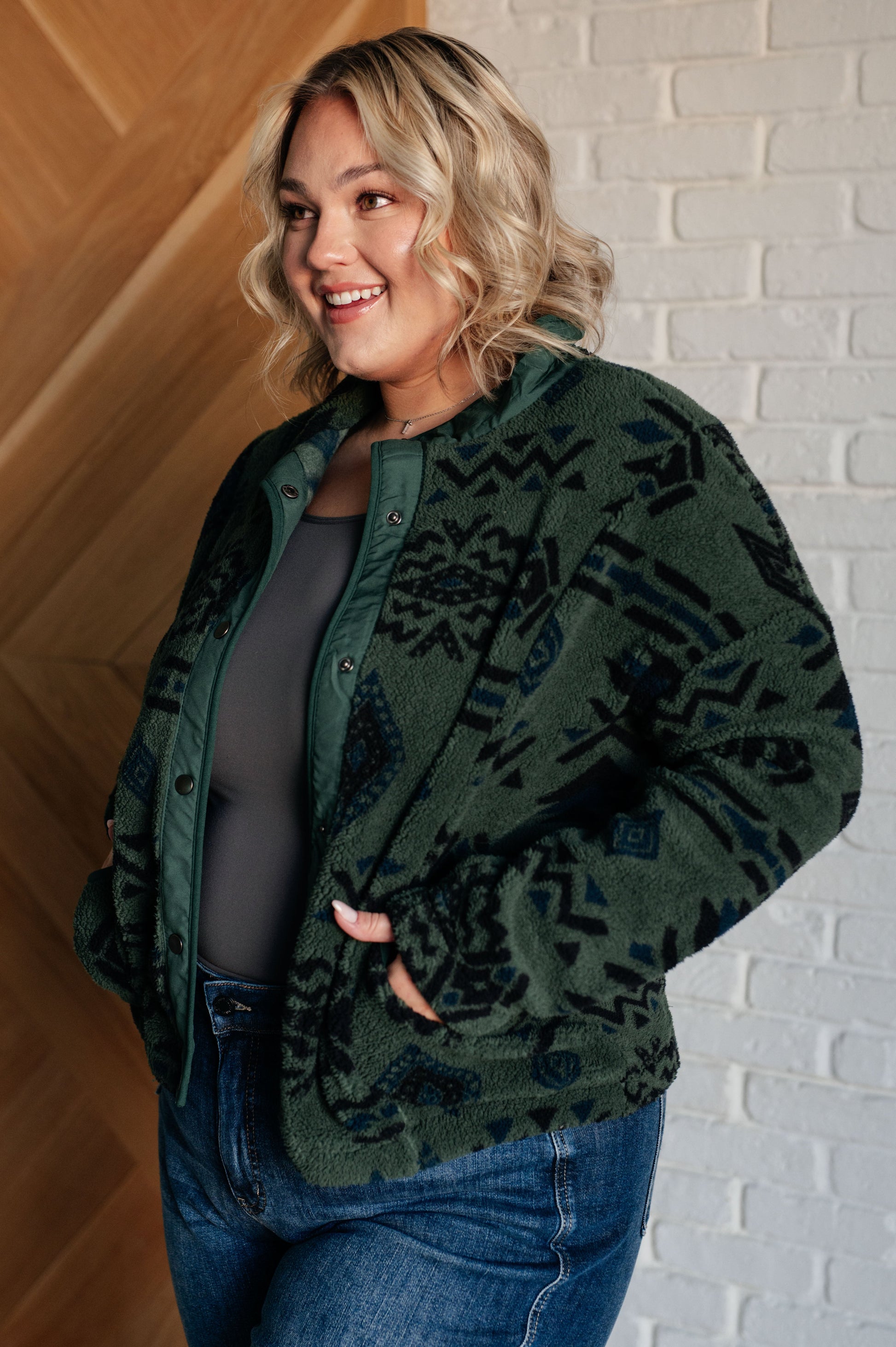 Woman wearing a green patterned jacket against a white brick wall.