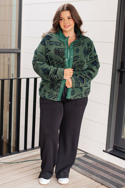 Woman wearing a green patterned jacket and black pants on a porch.