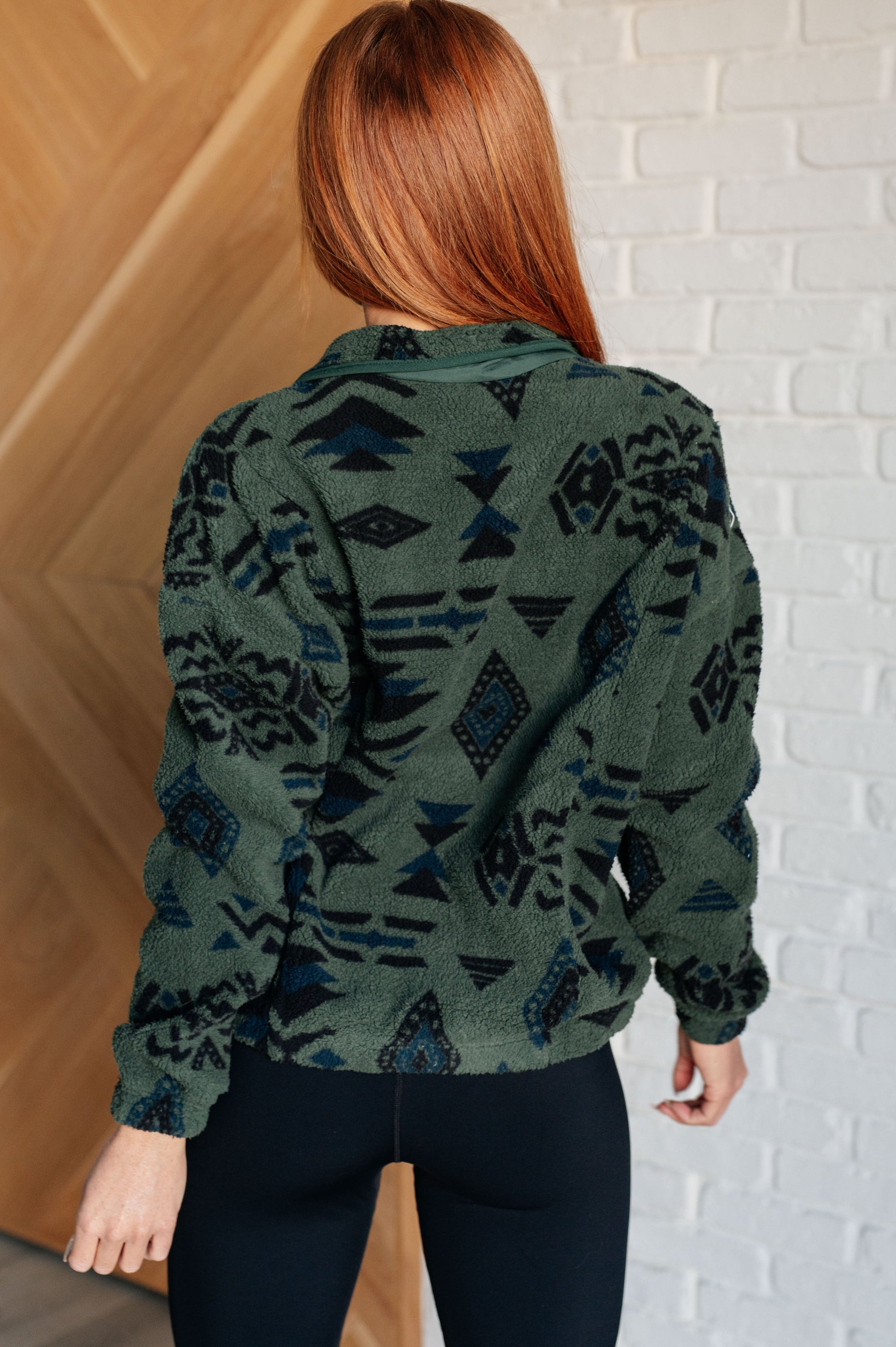 Person wearing a green patterned sweater against a white brick wall.