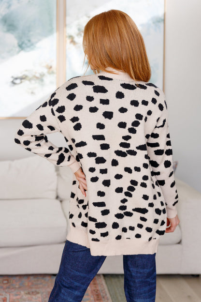 Person wearing a cream cardigan with black leopard print pattern in a living room setting.