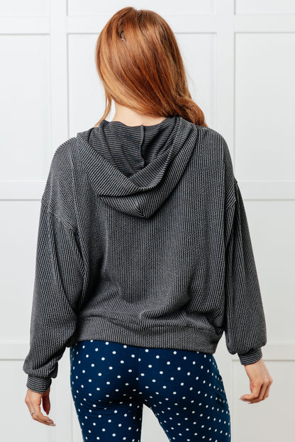 Person wearing a gray hooded sweater and blue polka dot pants against a white tiled wall.