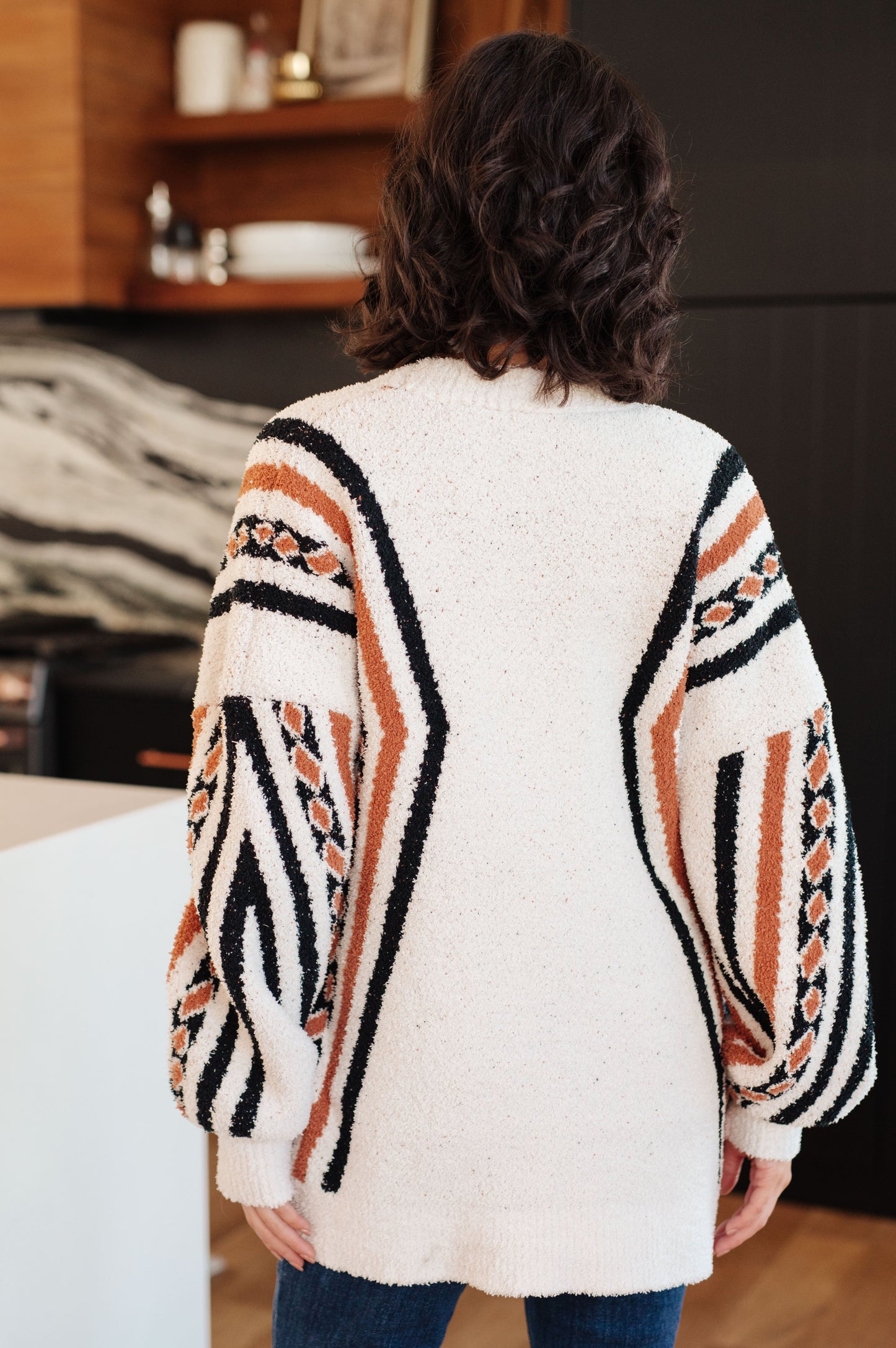 Person wearing a white cardigan with black and orange geometric patterns in a room.