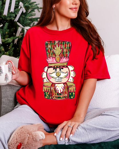 Person wearing a red t-shirt with a festive design, sitting in front of a Christmas tree.