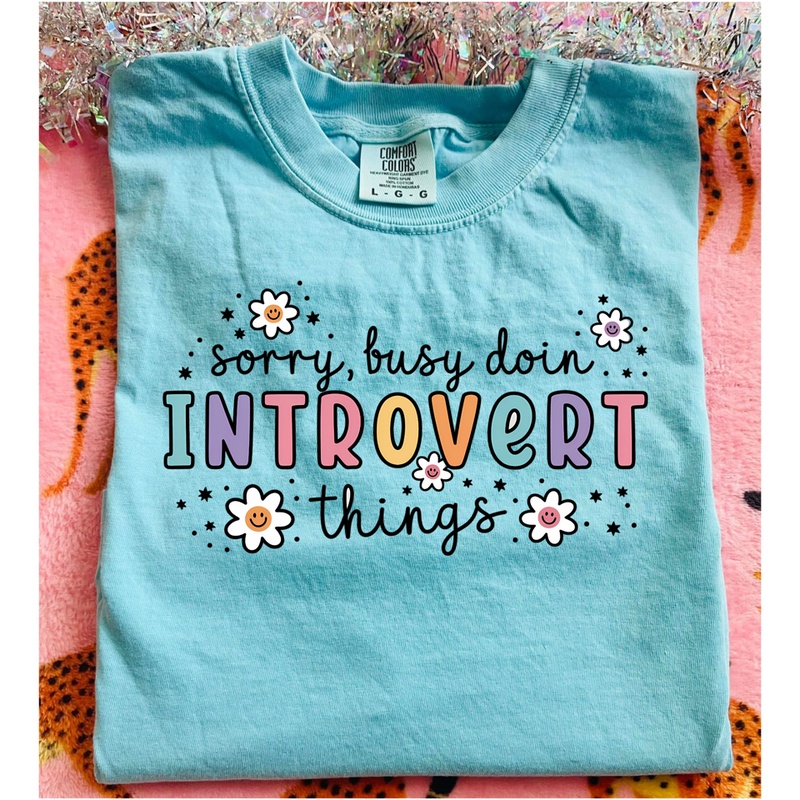 Light blue t-shirt with colorful text and flowers on a pink and orange patterned background