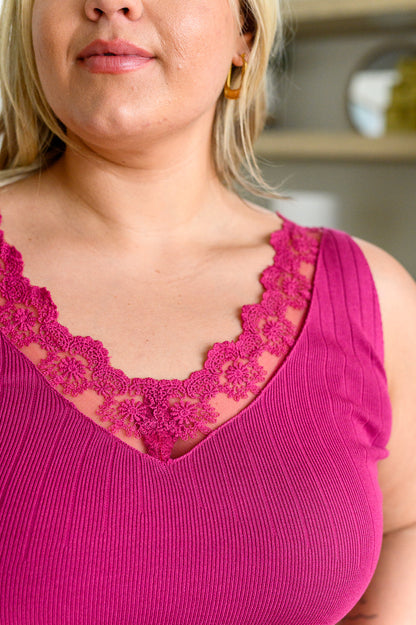 A woman wearing a berry-colored, lace-trimmed sleeveless tank top with a v-neckline, paired with white shorts.