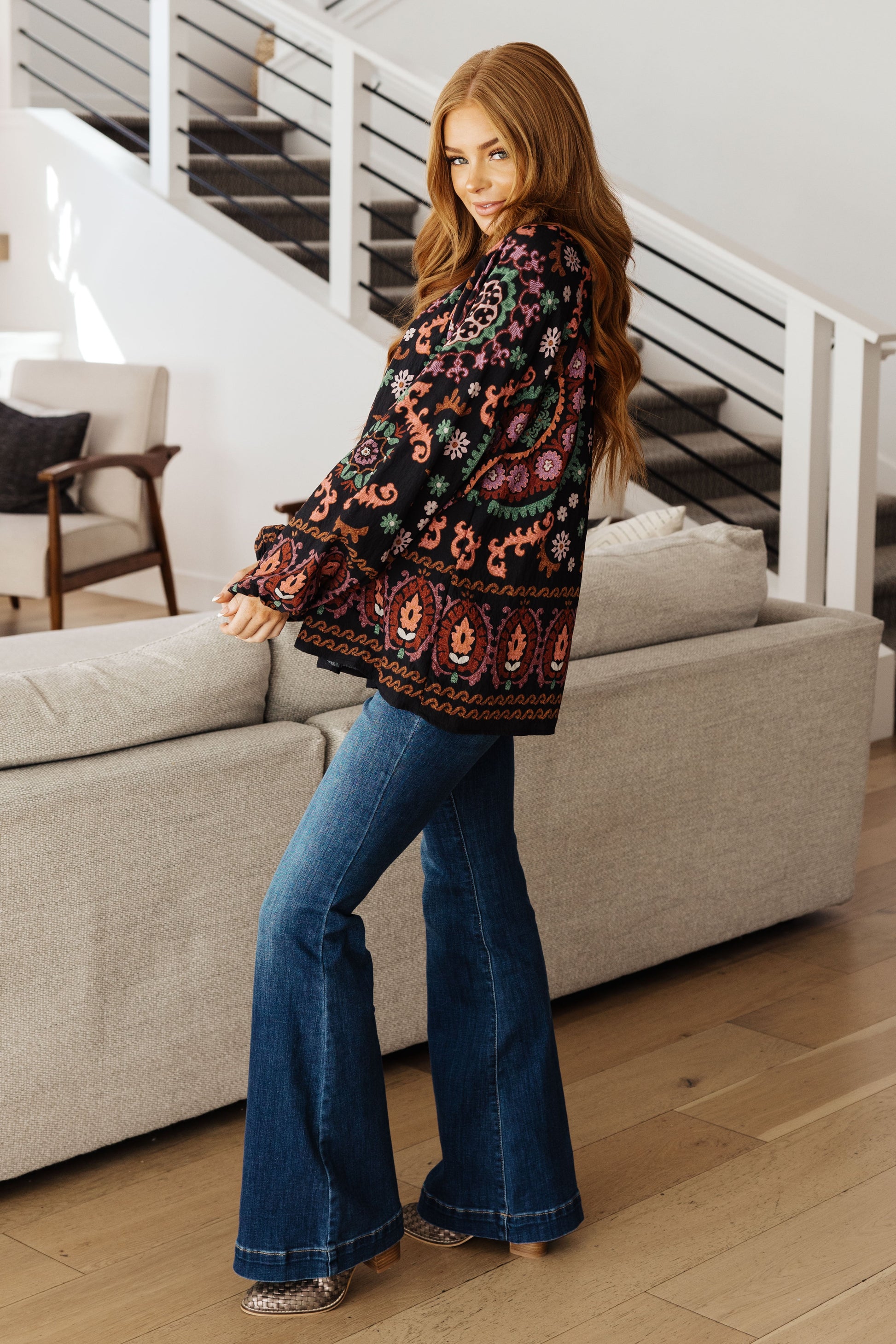 Woman wearing a patterned top and blue jeans in a living room setting