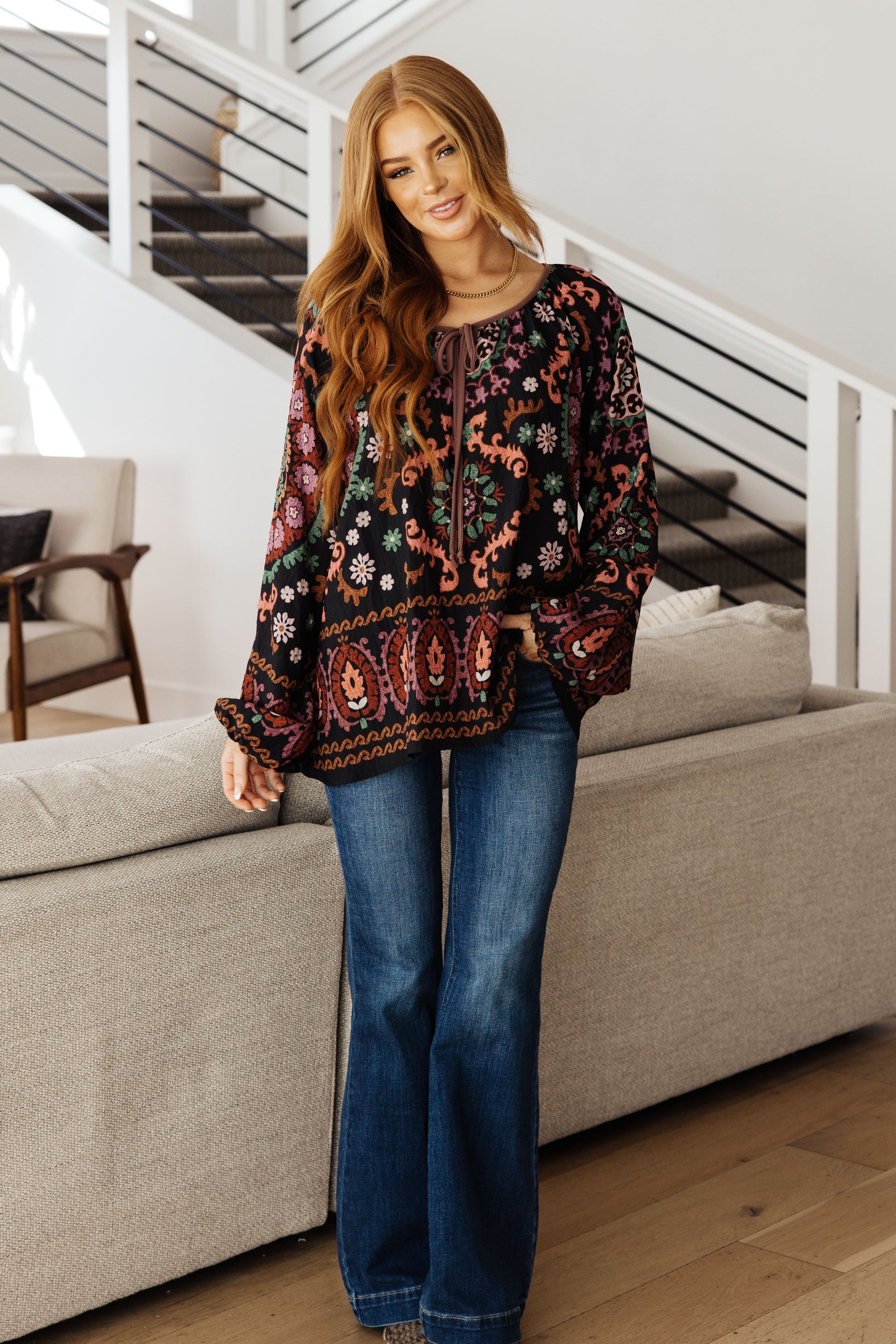 Woman wearing a patterned top and blue jeans in a living room setting