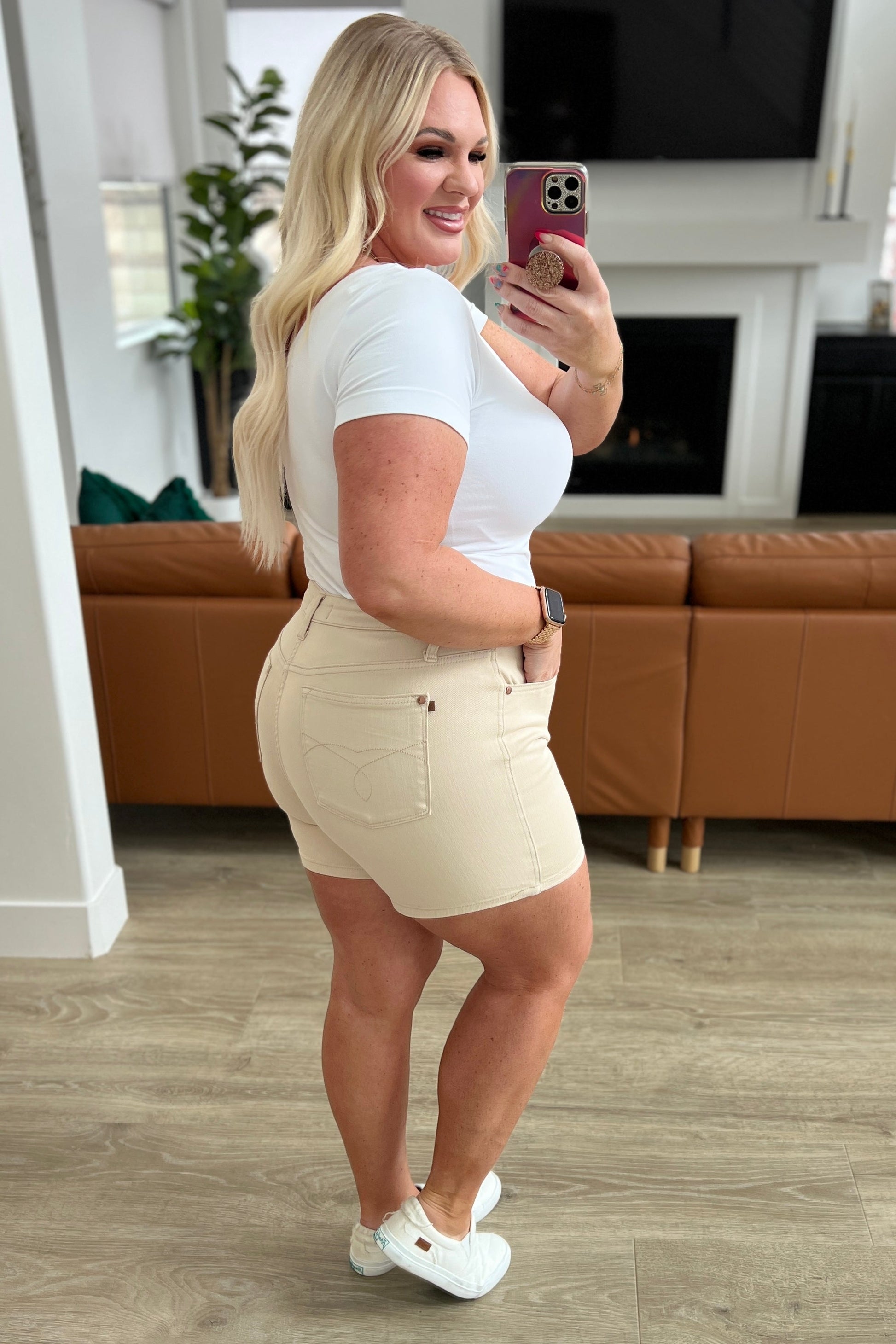 A woman is standing in a room wearing beige high-rise garment dyed shorts and a gray sleeveless 