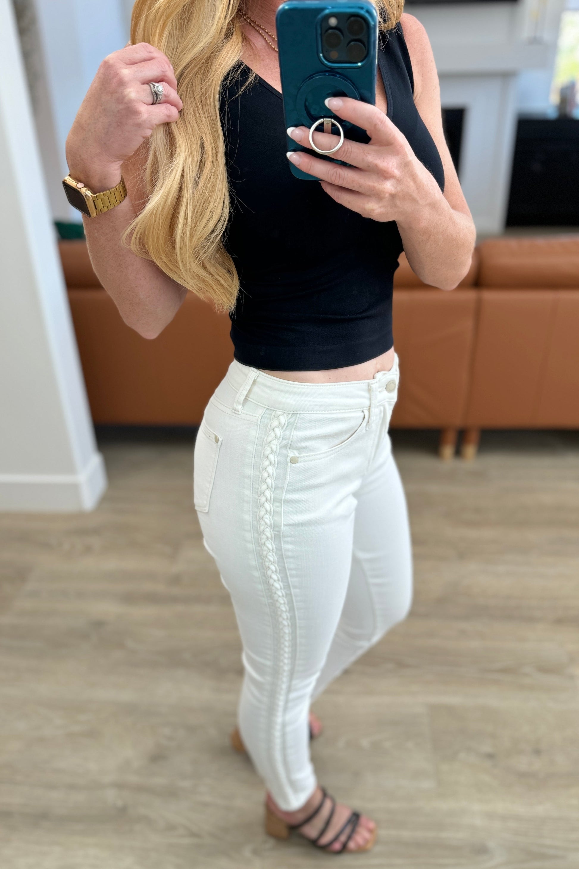 Person taking a mirror selfie wearing a black top and white pants in a room with wooden flooring.