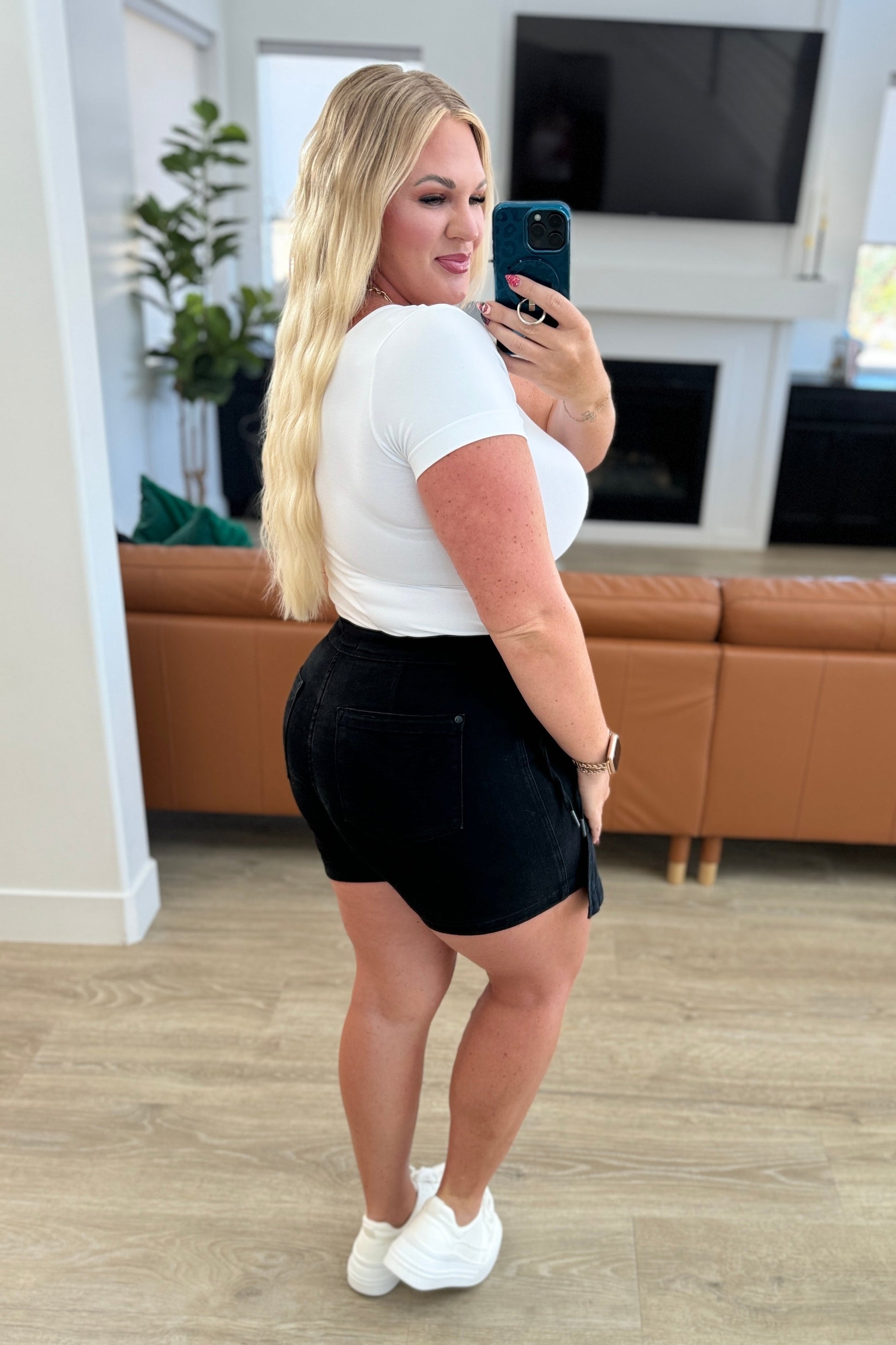 A person wearing a high rise side tie denim skort in black color with a self-tie side closure.