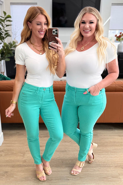 Two women taking a selfie wearing white tops and teal pants in a living room.