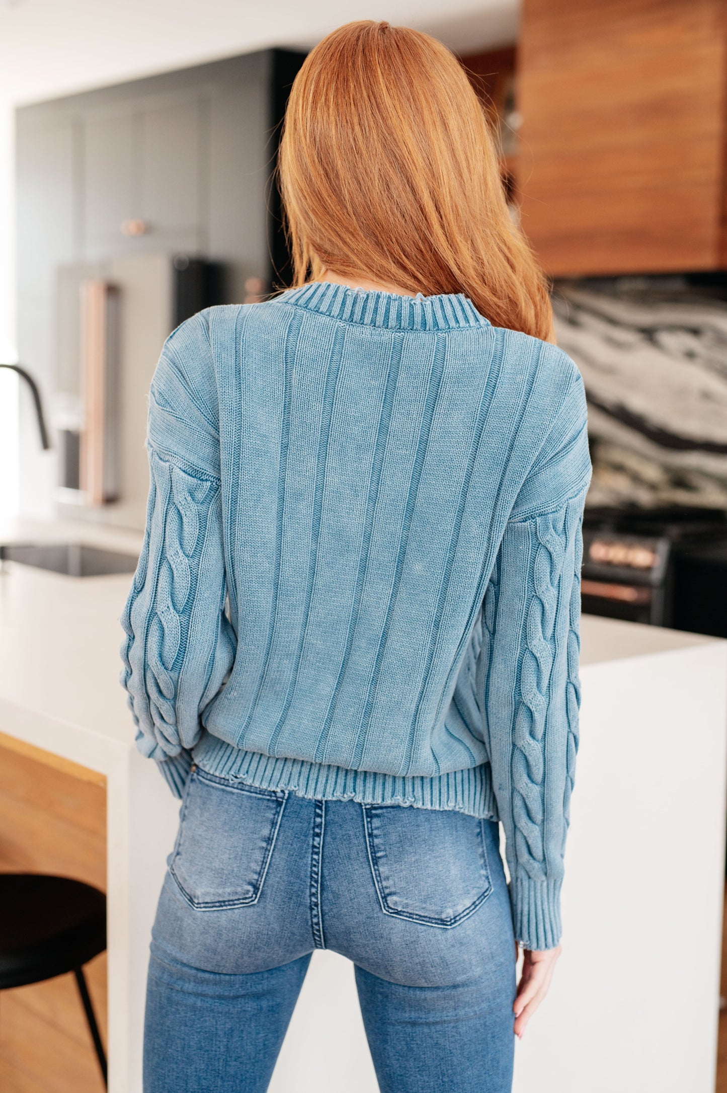 Person wearing a blue cable knit sweater and jeans in a kitchen setting