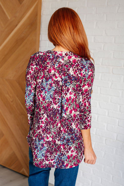 Woman wearing a colorful floral blouse against a white brick wall.