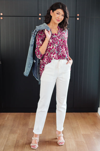 Woman wearing a floral blouse and white pants in a room with dark paneled walls.