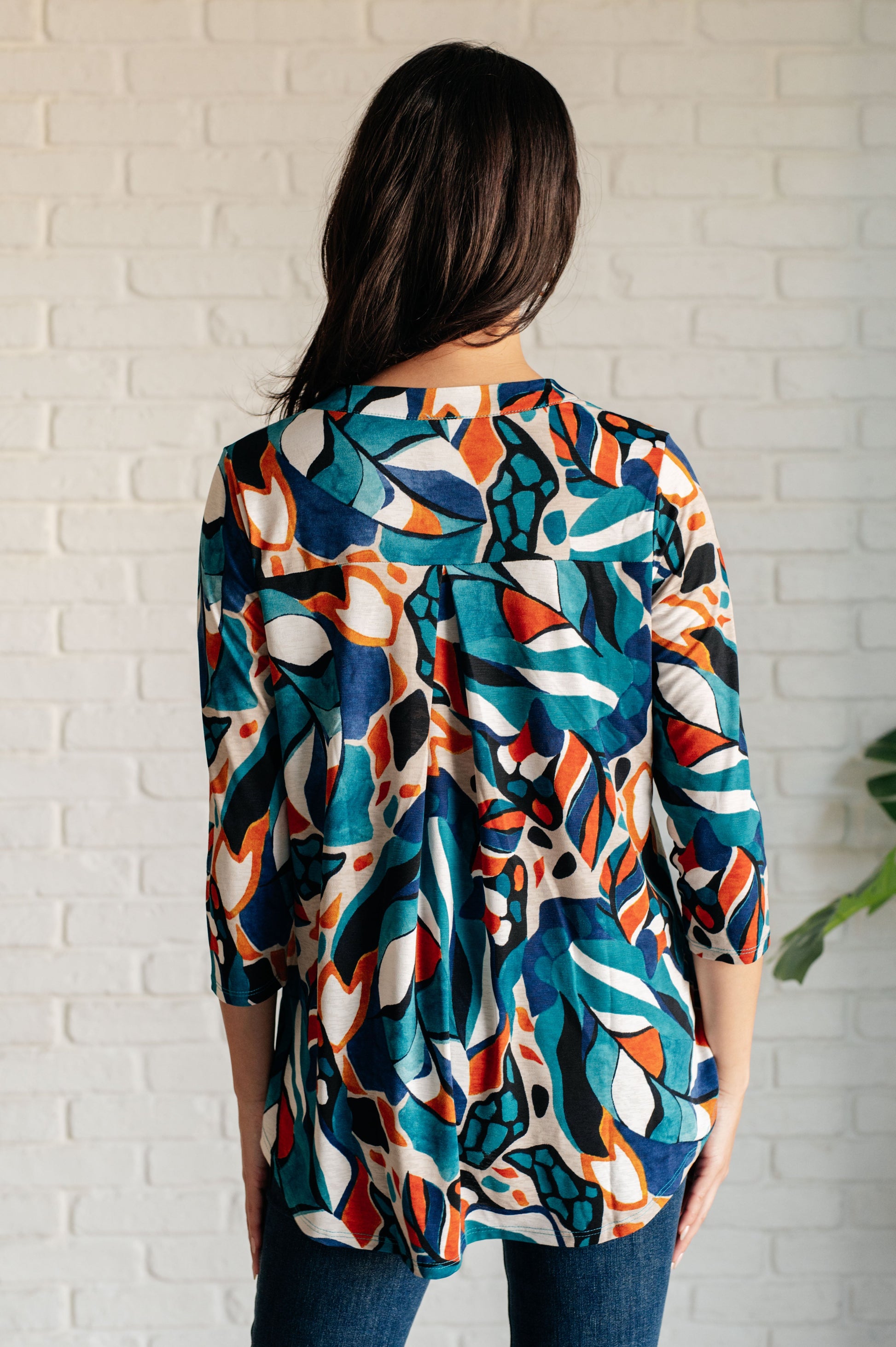 Person wearing a colorful patterned shirt against a white brick wall.