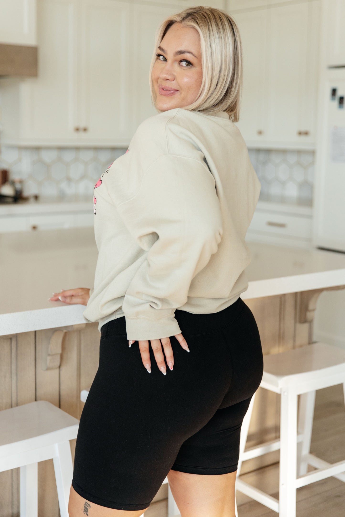 Woman in a beige hoodie and black shorts standing in a kitchen.
