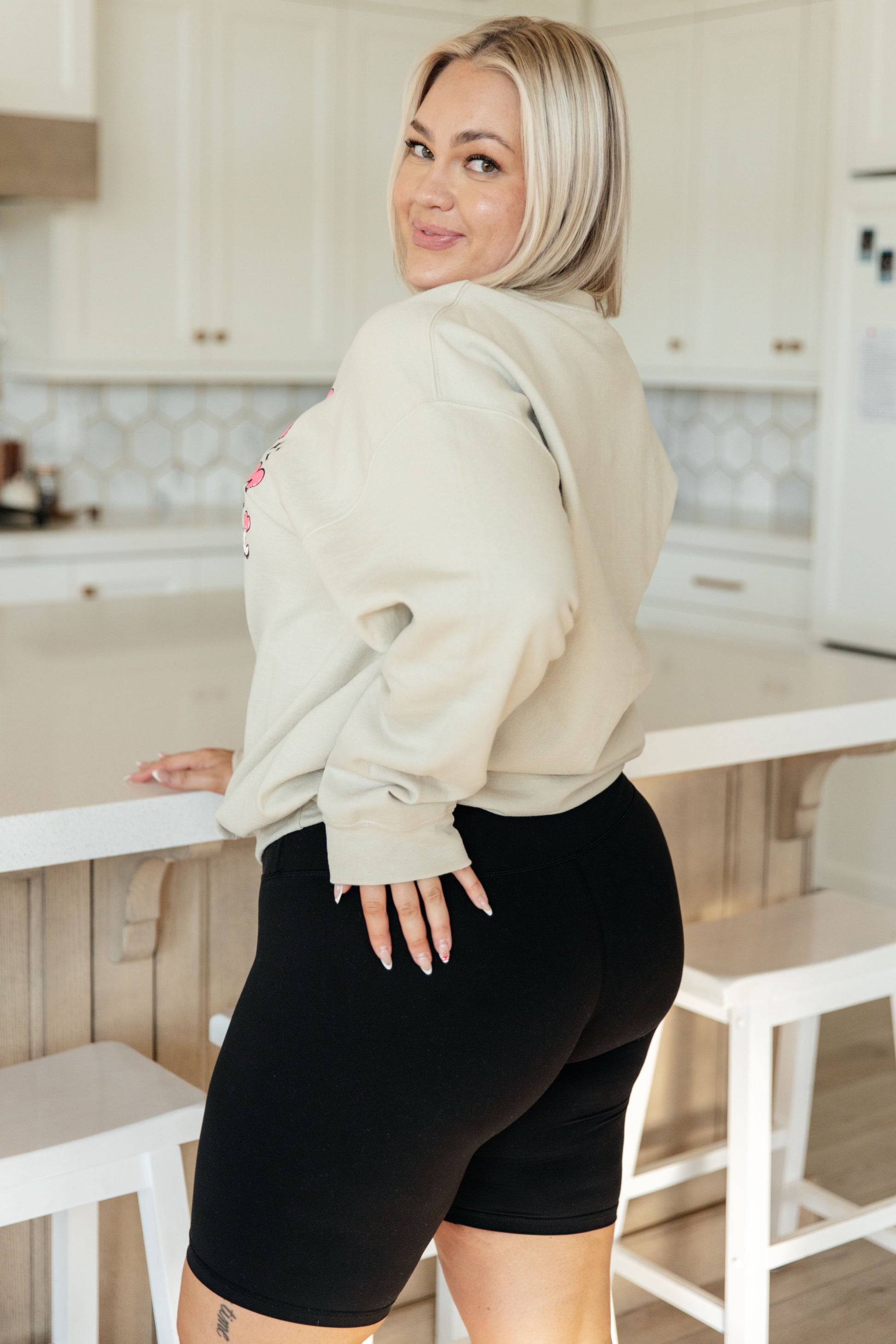 Woman in a beige hoodie and black shorts standing in a kitchen.