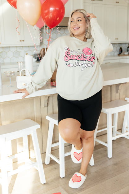 Woman in a kitchen wearing a sweatshirt with a heart design, standing near balloons.