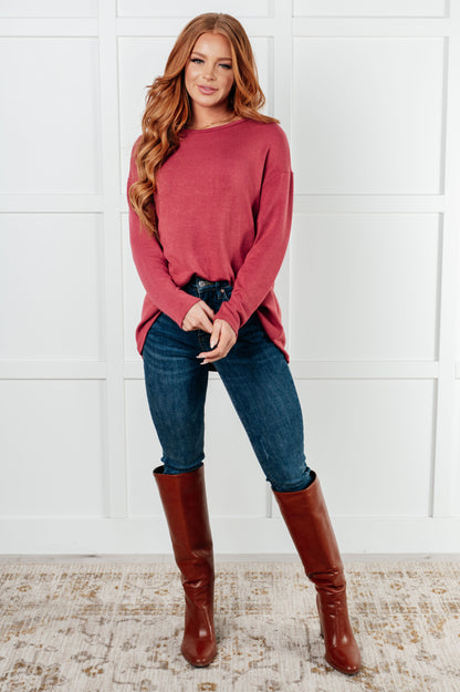Woman wearing a red sweater, blue jeans, and brown knee-high boots against a white wall.