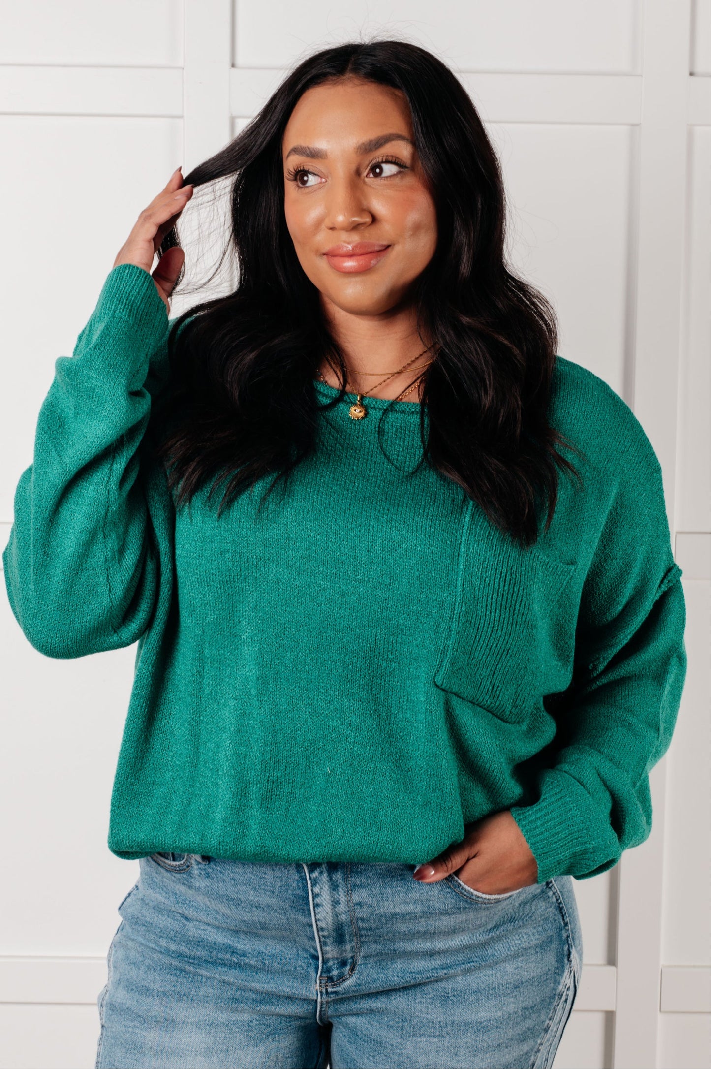 Woman wearing a teal sweater and jeans against a white wall
