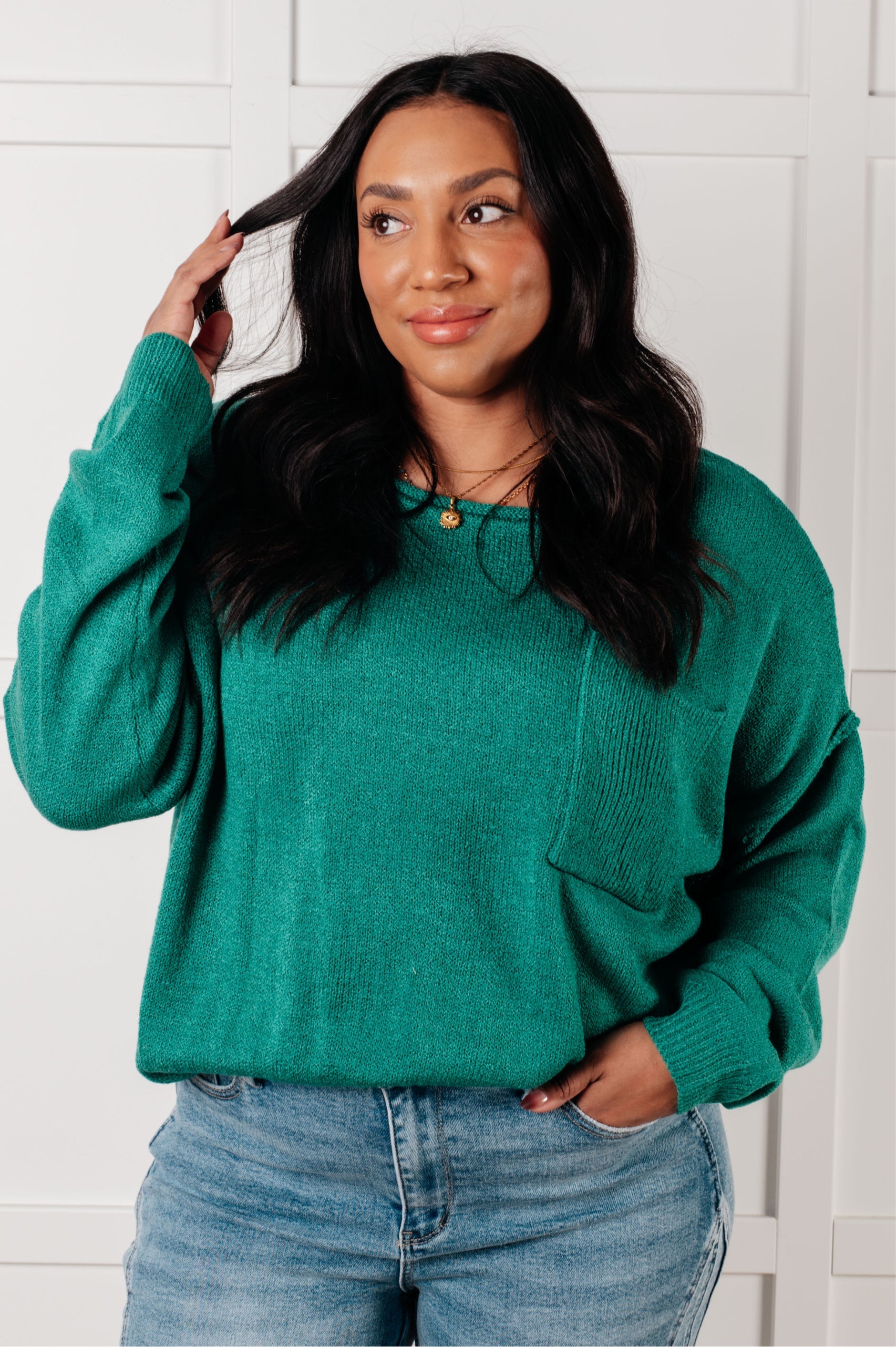 Woman wearing a teal sweater and jeans against a white wall