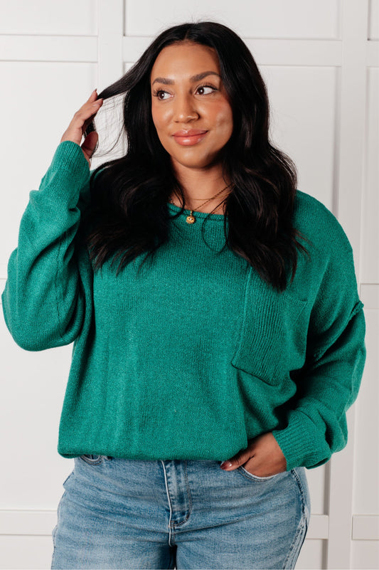 Woman wearing a teal sweater and jeans against a white wall